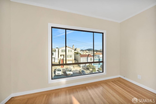 empty room with crown molding, baseboards, and wood finished floors