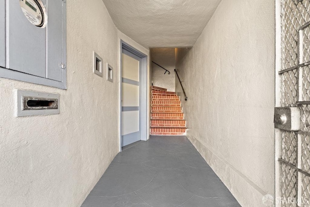 corridor featuring electric panel, concrete floors, a textured ceiling, and a textured wall