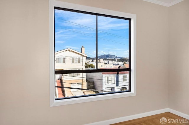 empty room with ornamental molding, wood finished floors, a mountain view, and baseboards