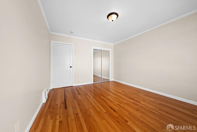 unfurnished bedroom featuring visible vents, baseboards, wood finished floors, crown molding, and a closet