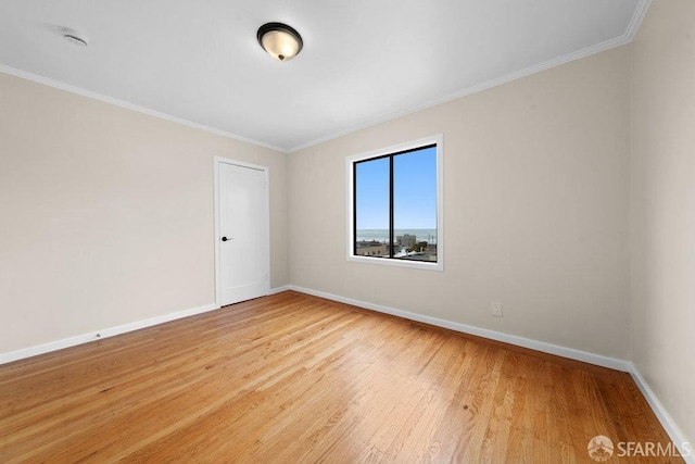 spare room with crown molding, light wood-style flooring, and baseboards