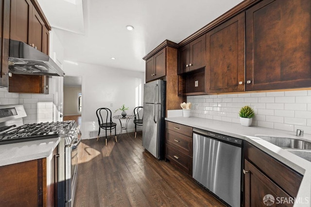 kitchen featuring stainless steel appliances, dark wood-style flooring, light countertops, and under cabinet range hood