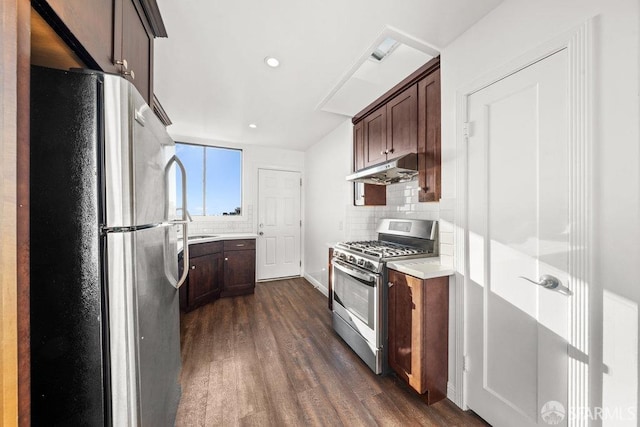 kitchen featuring dark wood-style flooring, stainless steel appliances, light countertops, backsplash, and under cabinet range hood