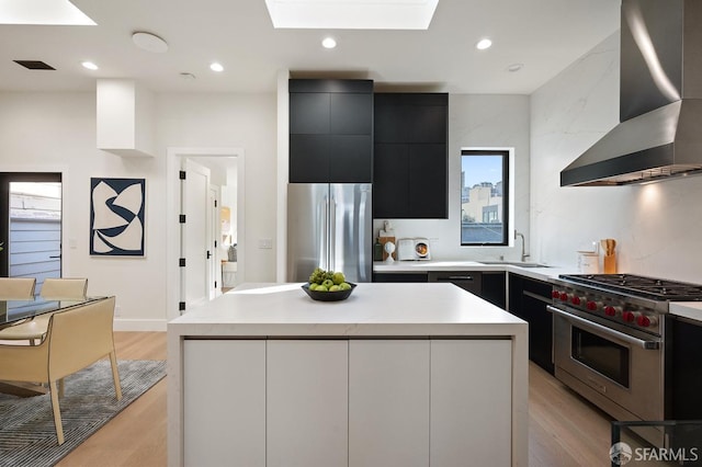 kitchen featuring appliances with stainless steel finishes, light countertops, a kitchen island, and wall chimney exhaust hood