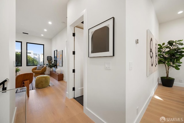 hall featuring baseboards, light wood-style flooring, and recessed lighting