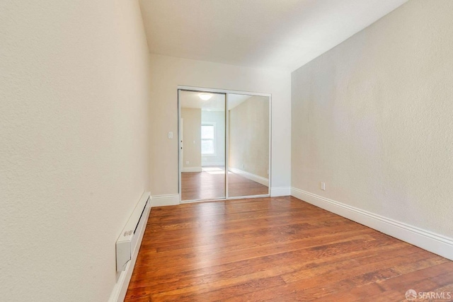 empty room featuring a baseboard heating unit, baseboards, and wood finished floors