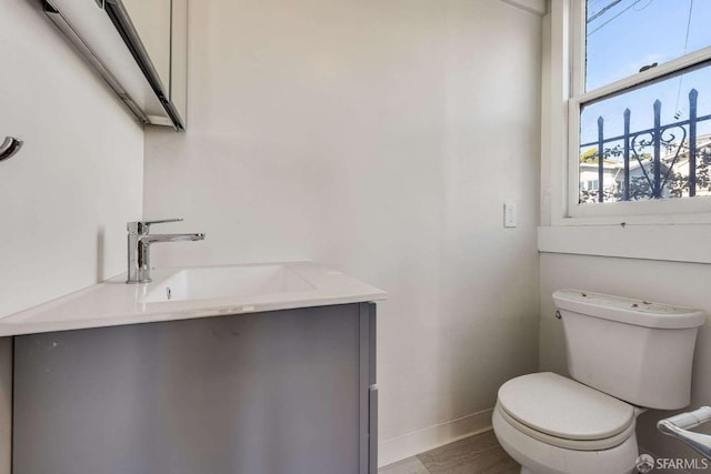 bathroom with toilet, wood finished floors, vanity, and baseboards