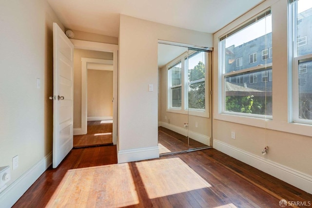 unfurnished bedroom with multiple windows, baseboards, and dark wood finished floors