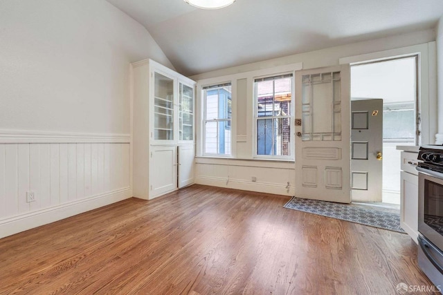 entryway featuring light wood-type flooring, vaulted ceiling, and a wainscoted wall