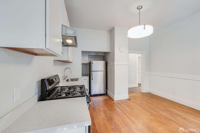 kitchen featuring freestanding refrigerator, white cabinets, light countertops, a sink, and gas range oven