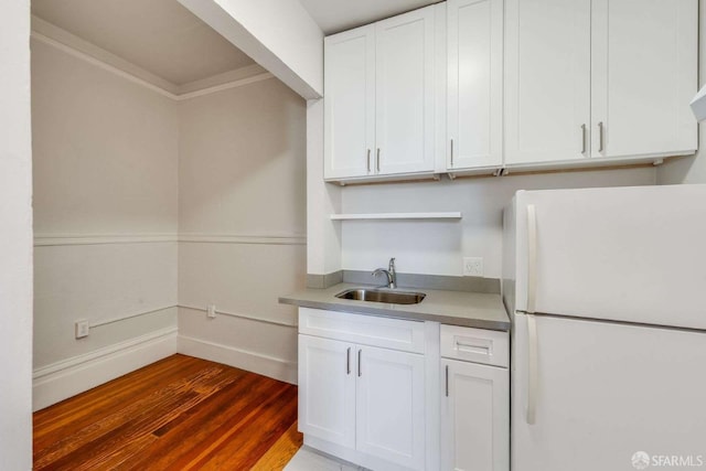 kitchen featuring baseboards, a sink, freestanding refrigerator, dark wood finished floors, and white cabinetry
