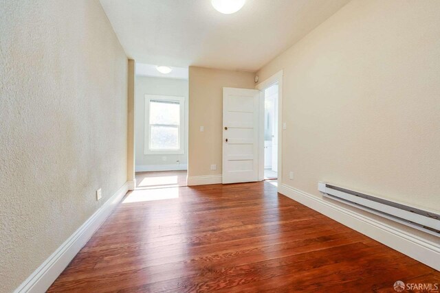 empty room with a textured wall, baseboards, a baseboard heating unit, and wood finished floors