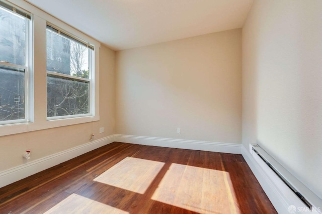 spare room featuring a baseboard radiator, baseboards, and wood finished floors