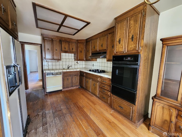 kitchen with tasteful backsplash, sink, tile counters, light hardwood / wood-style floors, and black appliances