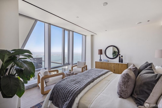 bedroom with light wood-type flooring, a water view, and expansive windows