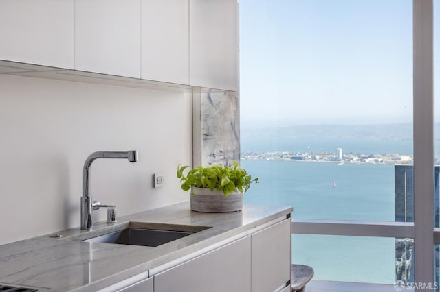 interior space with light stone countertops, sink, a water view, and white cabinetry