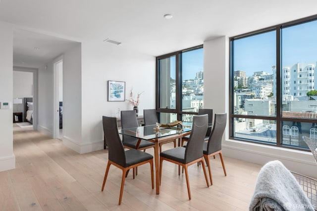 dining room featuring baseboards, a city view, visible vents, and light wood finished floors