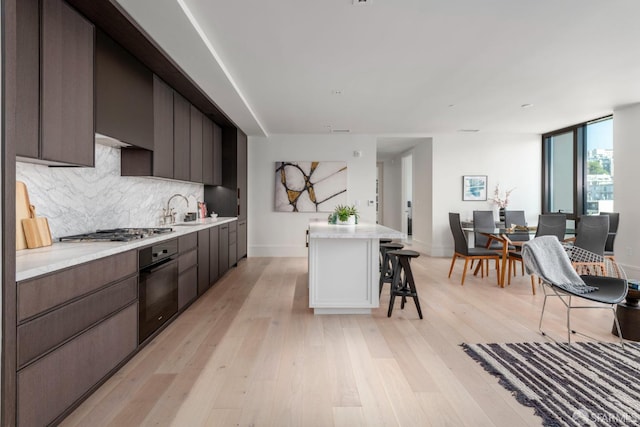 kitchen featuring light wood finished floors, stainless steel gas stovetop, decorative backsplash, black oven, and a kitchen bar