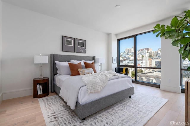 bedroom featuring light wood-style floors, a view of city, and baseboards