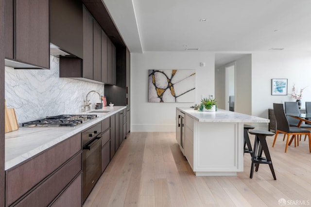 kitchen featuring decorative backsplash, a breakfast bar, a center island, light wood-style floors, and black oven