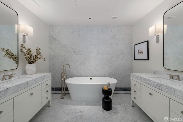 full bath with marble finish floor, two vanities, a soaking tub, and a sink