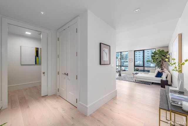 hallway featuring a wall of windows, light wood-type flooring, and baseboards