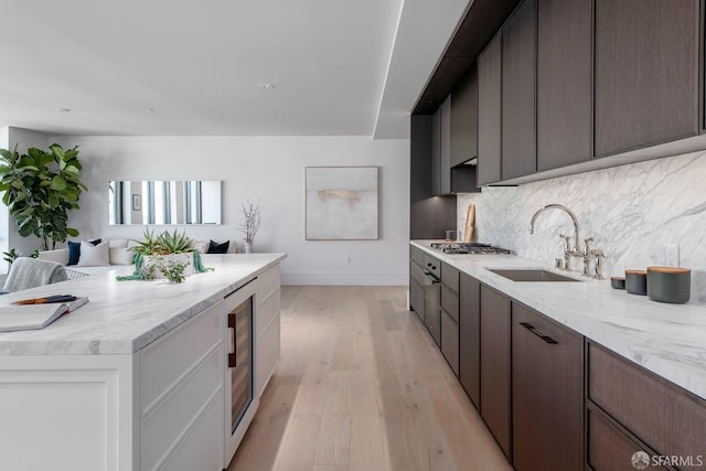 kitchen with wine cooler, stainless steel gas stovetop, backsplash, a sink, and light wood-type flooring