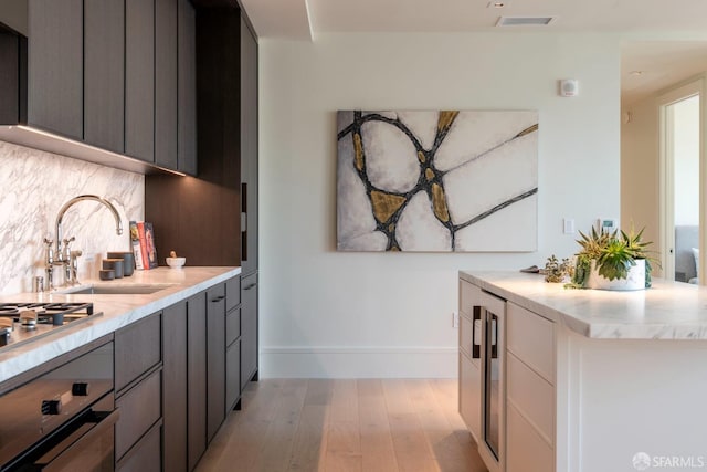 kitchen with tasteful backsplash, stainless steel gas stovetop, wall oven, a sink, and light wood-type flooring