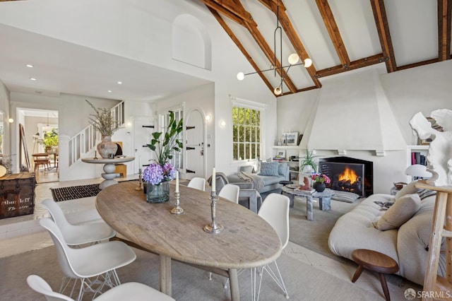 dining room with beamed ceiling, high vaulted ceiling, a notable chandelier, stairway, and a fireplace