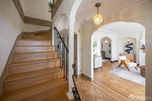 staircase with a textured ceiling, arched walkways, crown molding, baseboards, and a textured wall