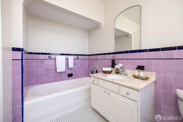 full bath featuring a wainscoted wall, toilet, vanity, a bathing tub, and tile walls