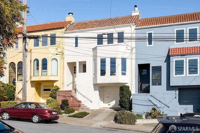 townhome / multi-family property featuring a tile roof, a chimney, and stucco siding