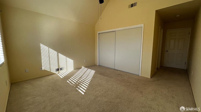 unfurnished bedroom featuring high vaulted ceiling, a closet, visible vents, and light colored carpet