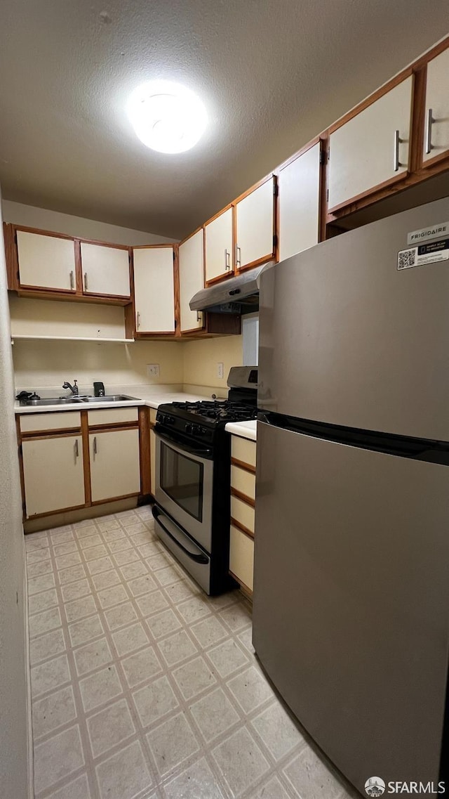 kitchen with under cabinet range hood, a sink, light countertops, appliances with stainless steel finishes, and light floors