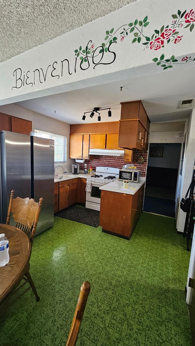 kitchen with white range with gas stovetop, brown cabinetry, light countertops, a peninsula, and freestanding refrigerator