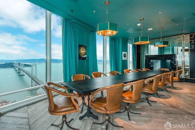 dining space featuring parquet floors, a fireplace, floor to ceiling windows, a water view, and a chandelier