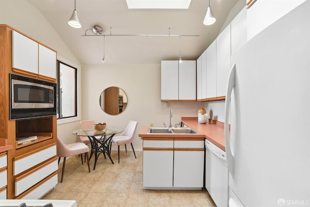 kitchen featuring vaulted ceiling with skylight, hanging light fixtures, a sink, white appliances, and white cabinetry