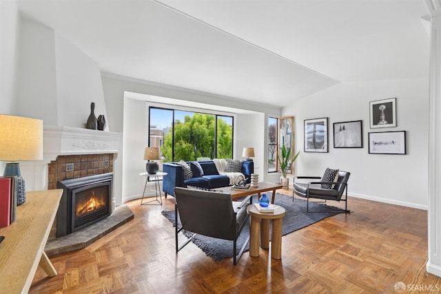 living room with a tiled fireplace, baseboards, and lofted ceiling