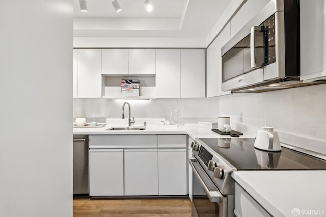 kitchen with light wood finished floors, a sink, appliances with stainless steel finishes, white cabinets, and open shelves