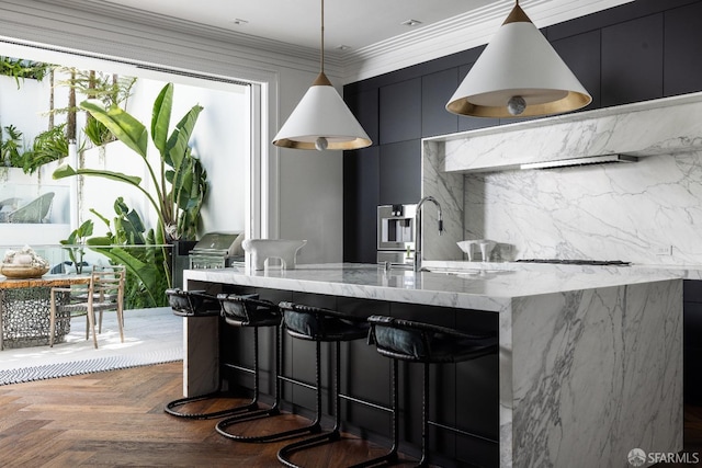 kitchen featuring sink, a breakfast bar, hanging light fixtures, light stone counters, and dark parquet flooring