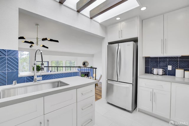 kitchen with stainless steel fridge, tasteful backsplash, white cabinets, sink, and a notable chandelier