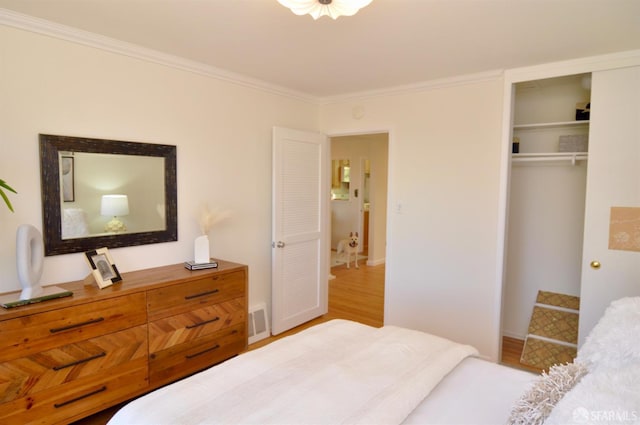 bedroom featuring a closet, baseboards, wood finished floors, and crown molding