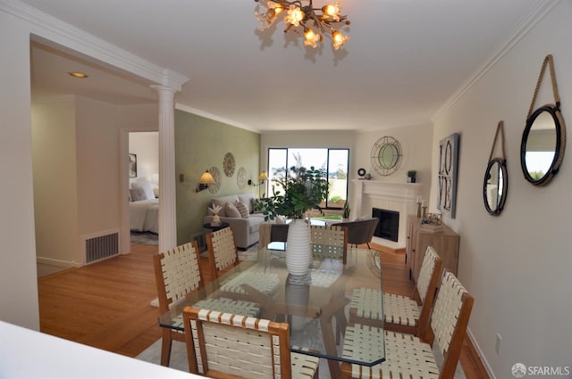 dining space with visible vents, a fireplace with raised hearth, crown molding, an inviting chandelier, and wood finished floors