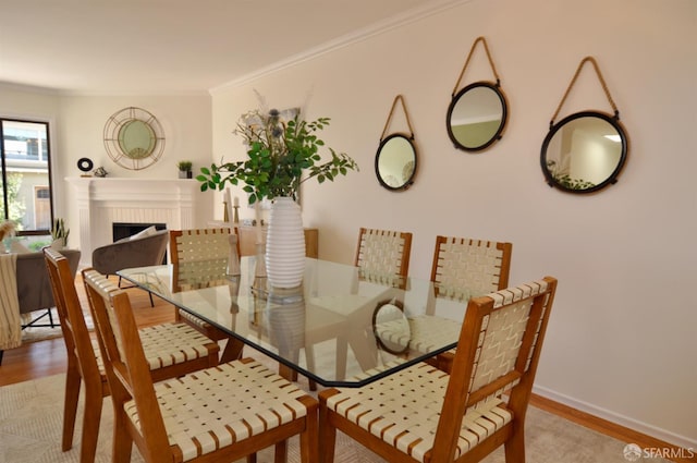 dining area featuring a fireplace, light wood-style flooring, and crown molding