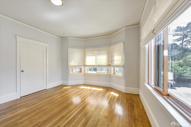 unfurnished room with crown molding, baseboards, and light wood-type flooring