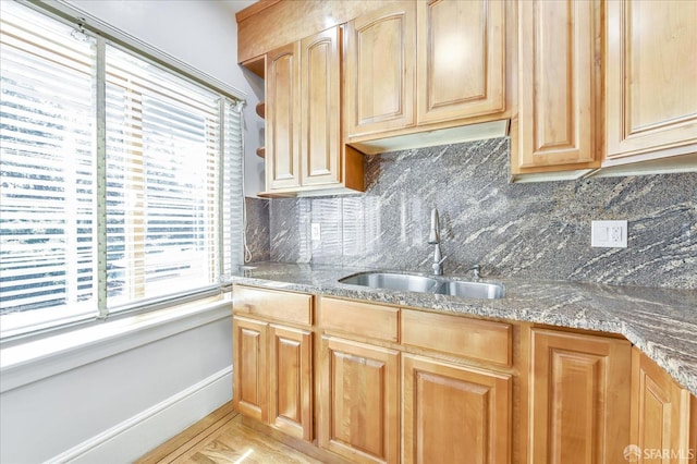 kitchen featuring tasteful backsplash, baseboards, a sink, and light brown cabinetry