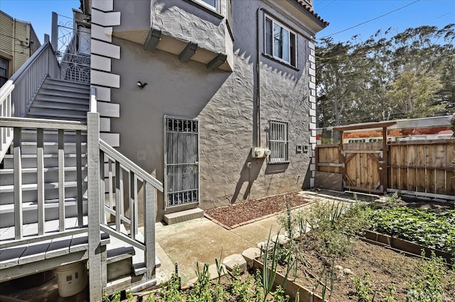back of property with stucco siding, fence, a vegetable garden, and stairway