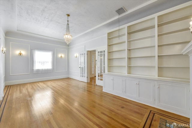unfurnished dining area with light wood-style floors, visible vents, a raised ceiling, french doors, and a notable chandelier