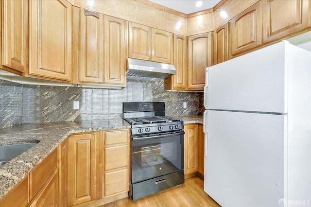 kitchen featuring black range with gas stovetop, light stone counters, freestanding refrigerator, under cabinet range hood, and light wood-style floors