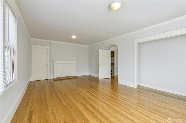 spare room featuring arched walkways, light wood-style floors, baseboards, and crown molding